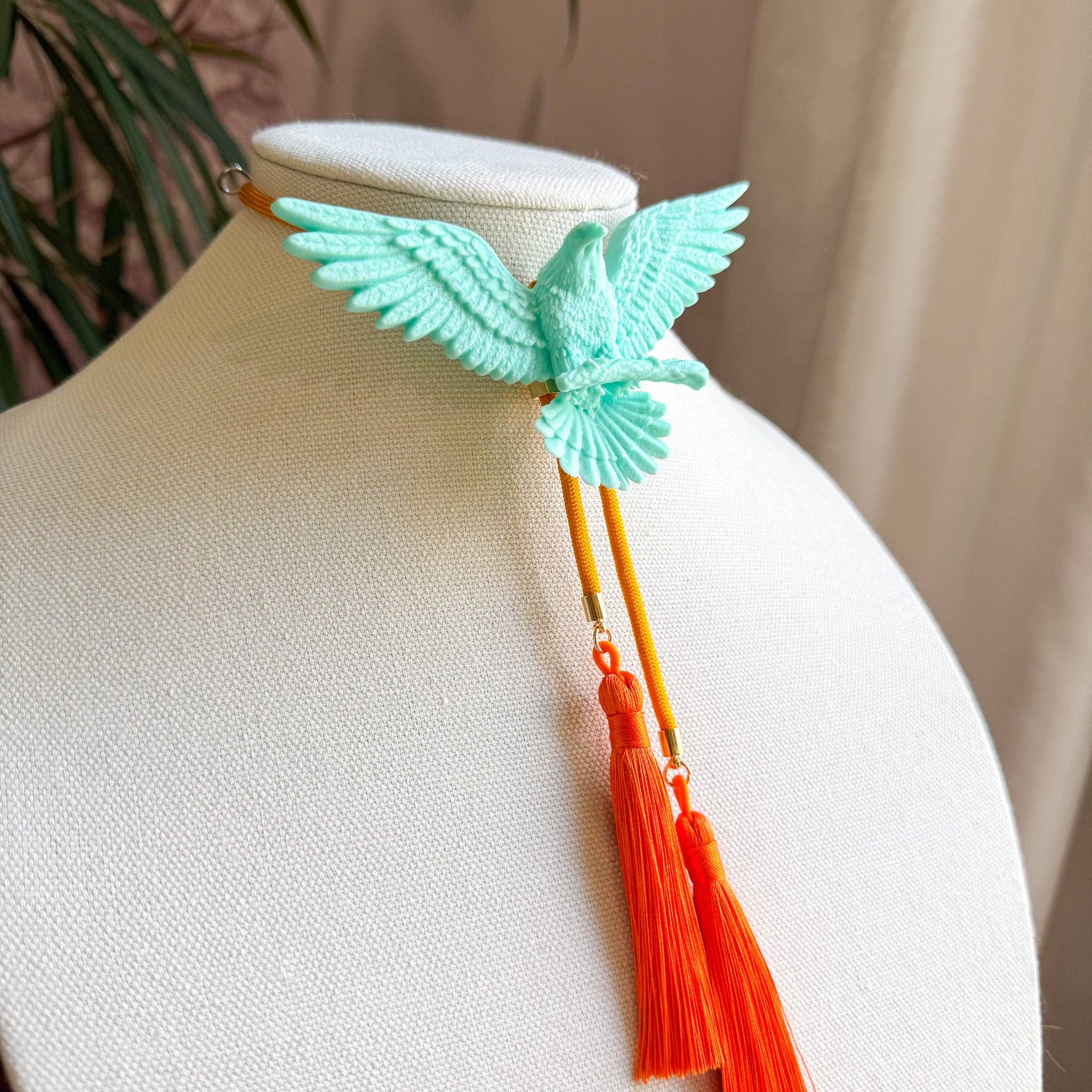 Eagle Bolo Turquoise with Golden Yellow & Orange displayed on a beige mannequin with vibrant orange tassels hanging down