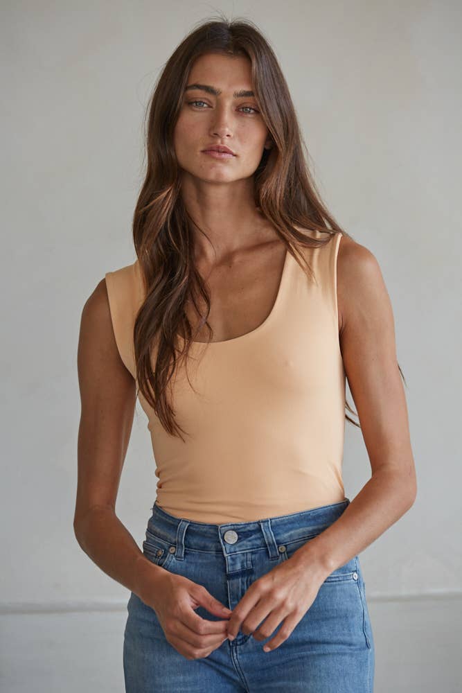 Woman wearing a beige Double Layered Seamless Top paired with blue jeans in a casual, minimalist setting.