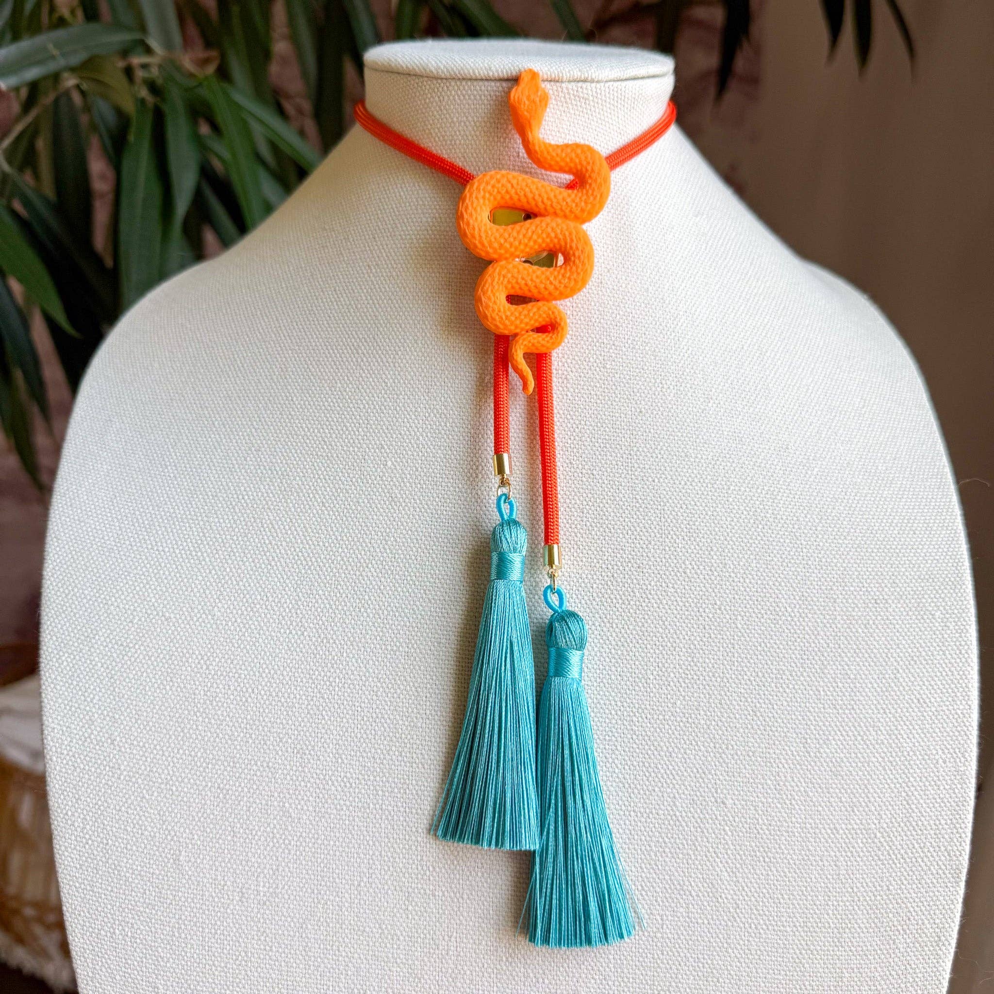 Snake Bolo Orange Citrus with Solar Orange & Lagoon Blue necklace featuring a bright orange snake and blue tassels on display bust