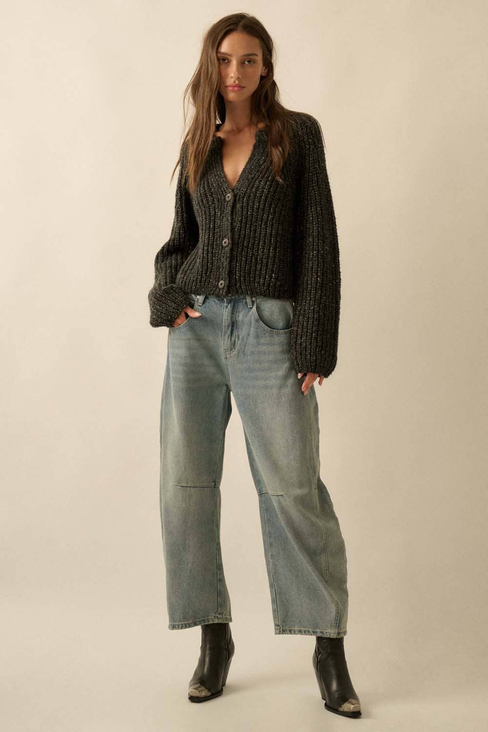 A woman with long brown hair and a neutral expression wears the Promesa USA Confetti Button-Front Cardigan Sweater, styled with loose light blue jeans and black ankle boots against a beige background.
