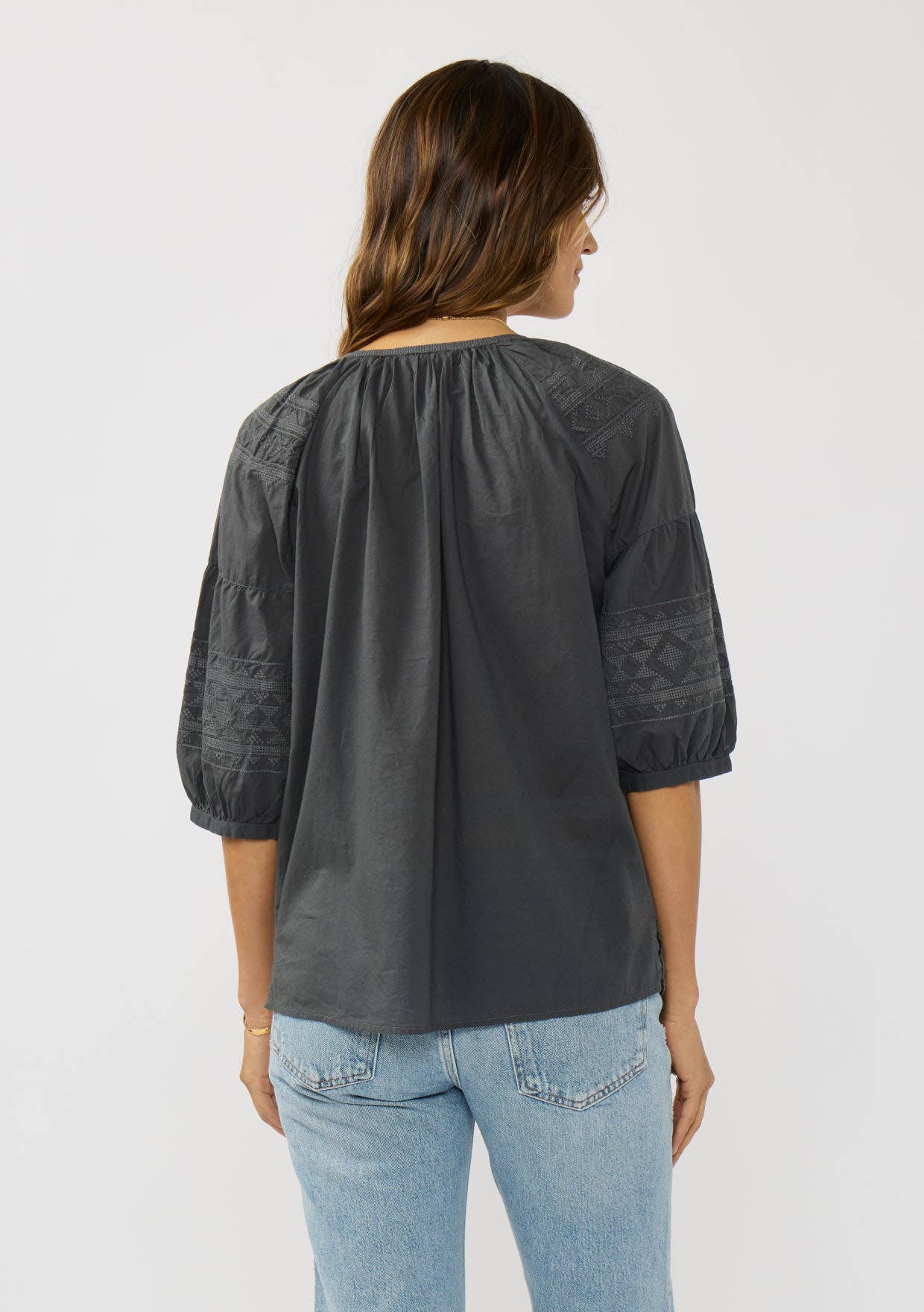 Woman wearing a charcoal Short Raglan Puff Sleeve Button Down Top with embroidered sleeves and light wash jeans viewed from back